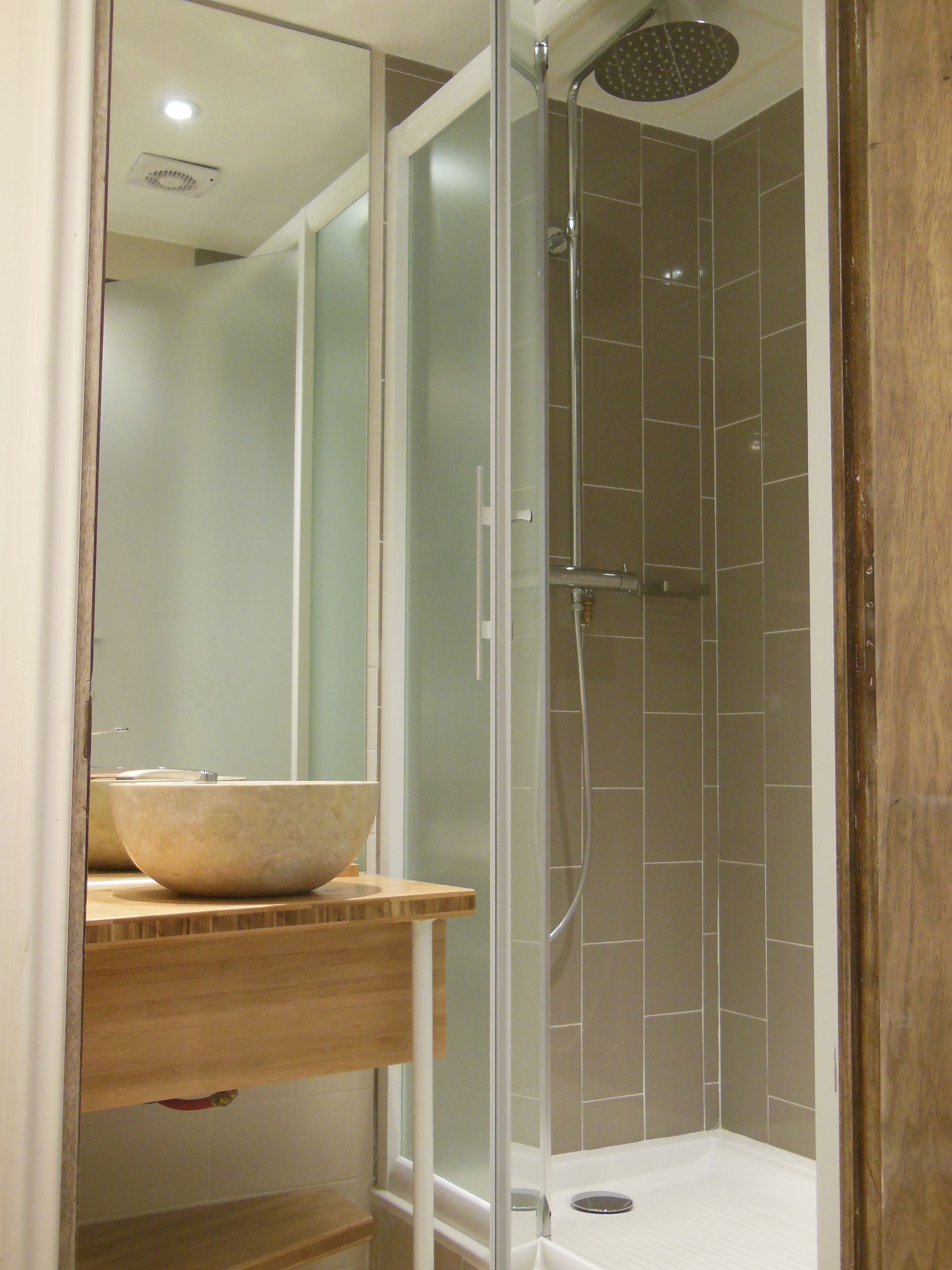A bathroom with a glass-enclosed shower, a wooden vanity with a bowl sink, and a mirror.