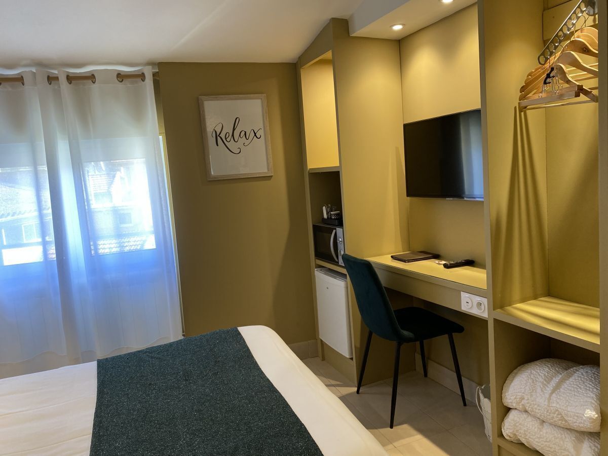 Ett hotellrum med en säng, ett skrivbord, en stol, en tv och en hylla med handdukar.