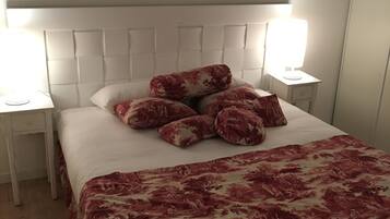 Una cama bien tendida con una colcha estampada con motivos florales, dos lámparas de noche y un cabecero con diseño de panel cuadrado.