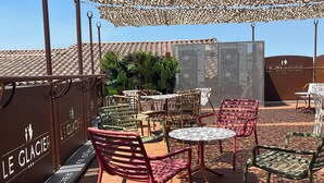 An outdoor seating area with tables and chairs, a shaded canopy, and a sign reading 'LE GLACIER'. - Logis Hôtel Le Glacier (Orange)