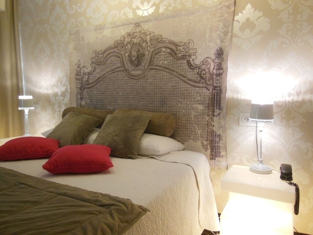 Una cama bien hecha con un cabecero decorativo, una lámpara de noche y un teléfono sobre una mesita de noche.