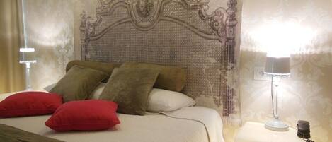 Una cama bien hecha con un cabecero decorativo, una lámpara de noche y un teléfono sobre una mesita de noche.