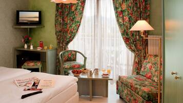 A hotel room with a bed, a desk with a chair, a television, and a window with curtains.