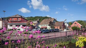 Un hôtel à la façade rouge, doté d’un balcon orné de fleurs rouges et d’une enseigne sur laquelle on peut lire « HÔTEL BUTTE ».