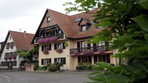 Un edificio tradizionale europeo con diversi balconi decorati da fiori, un ingresso centrale e vista sulla strada.