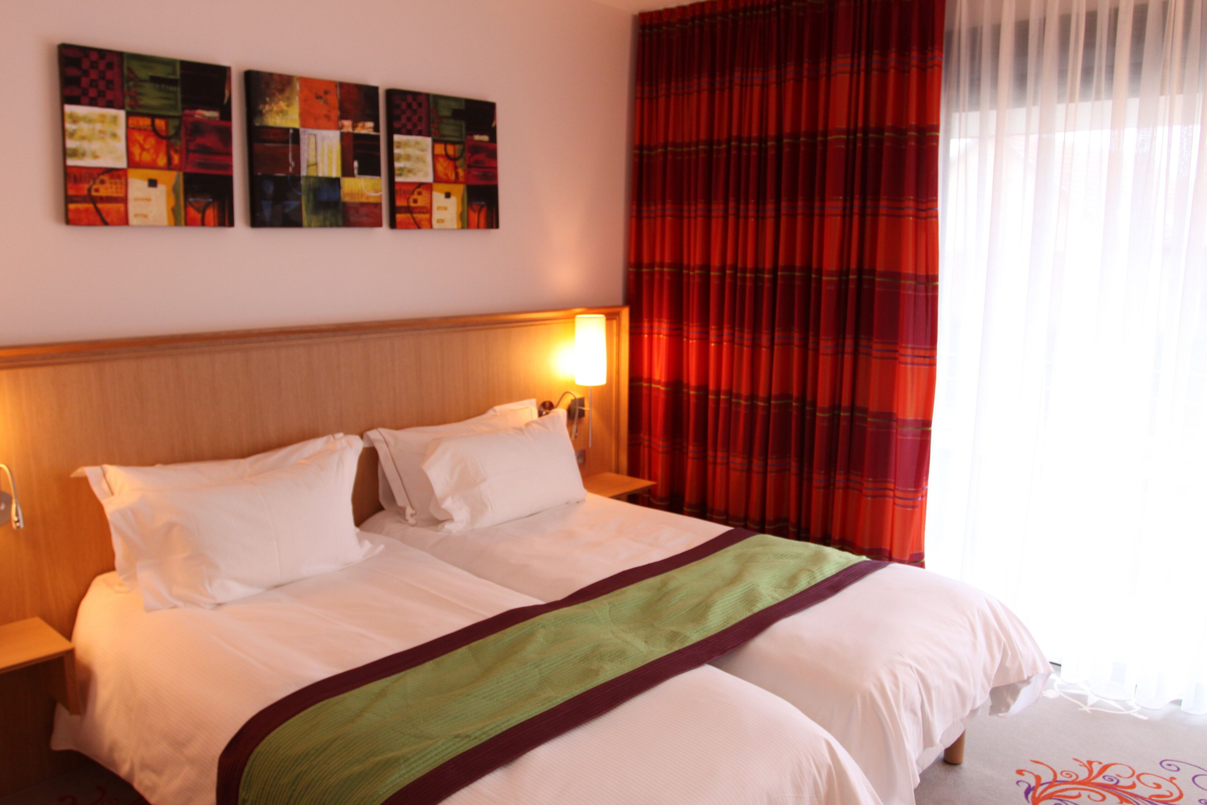 A hotel room with a large bed, a headboard, a nightstand, and a wall with three paintings.