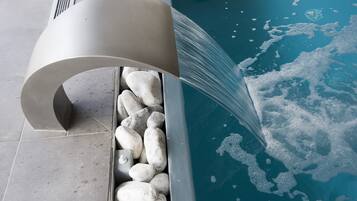 A modern pool with a curved water feature and white pebbles lining the edge.