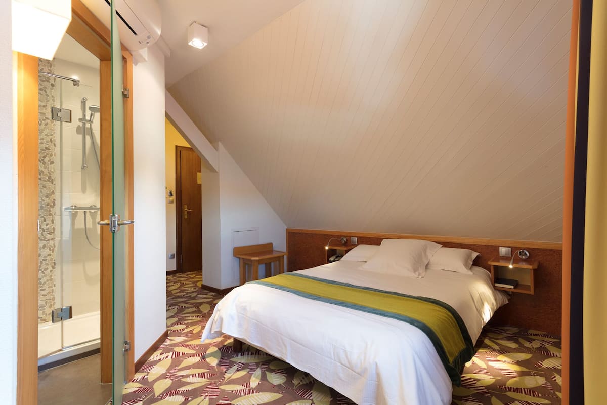 A bedroom with a bed, a nightstand, a bedside table, a glass shower enclosure, and a door.