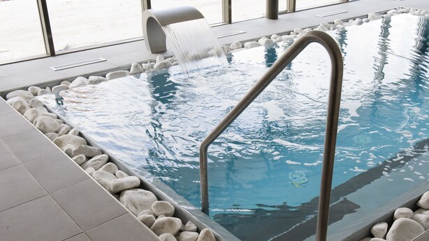 Una piscina interna con scala in metallo, circondata da ciottoli bianchi e pavimento piastrellato.