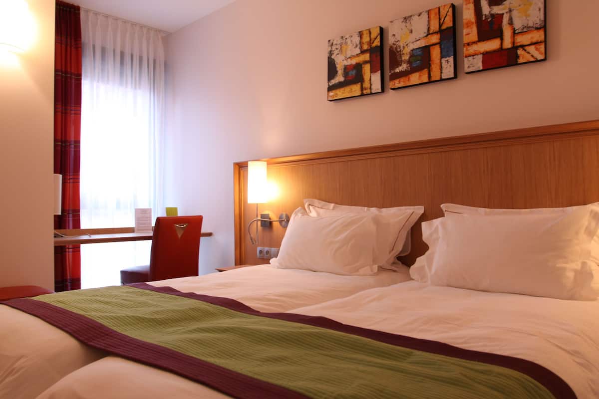 A hotel room with a bed, a desk, and a chair. There are three paintings on the wall.