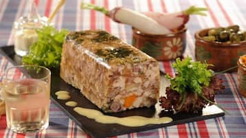 A terrine on a black plate with a side salad, a glass of water, and a bowl of grated carrots.