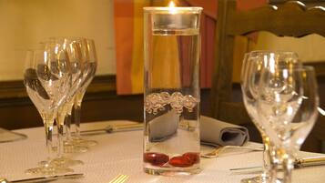 A table set with wine glasses, a candle, and a glass vase with red stones.