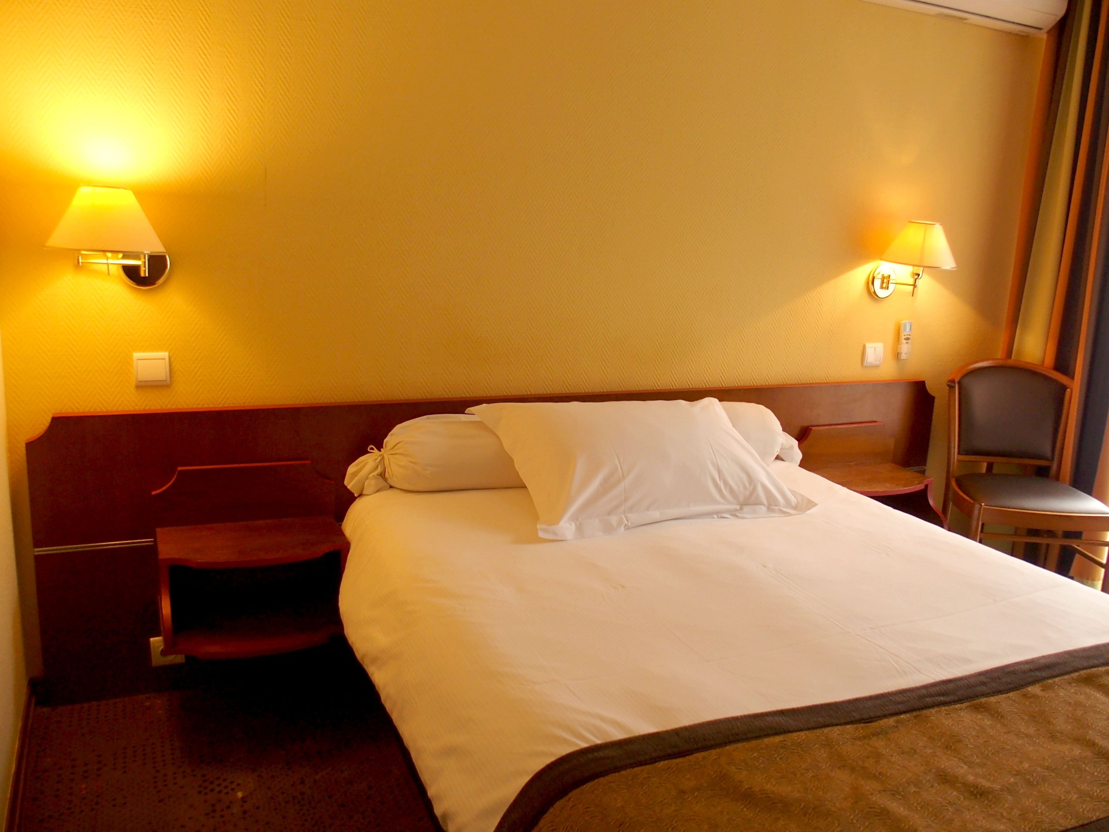 Una habitación de hotel con una cama grande, dos lámparas de noche, un cabecero de madera y una silla.