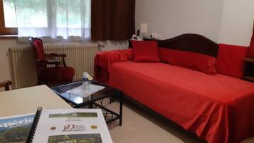 A room with a bed, a table with a book, a chair, and a window with curtains.