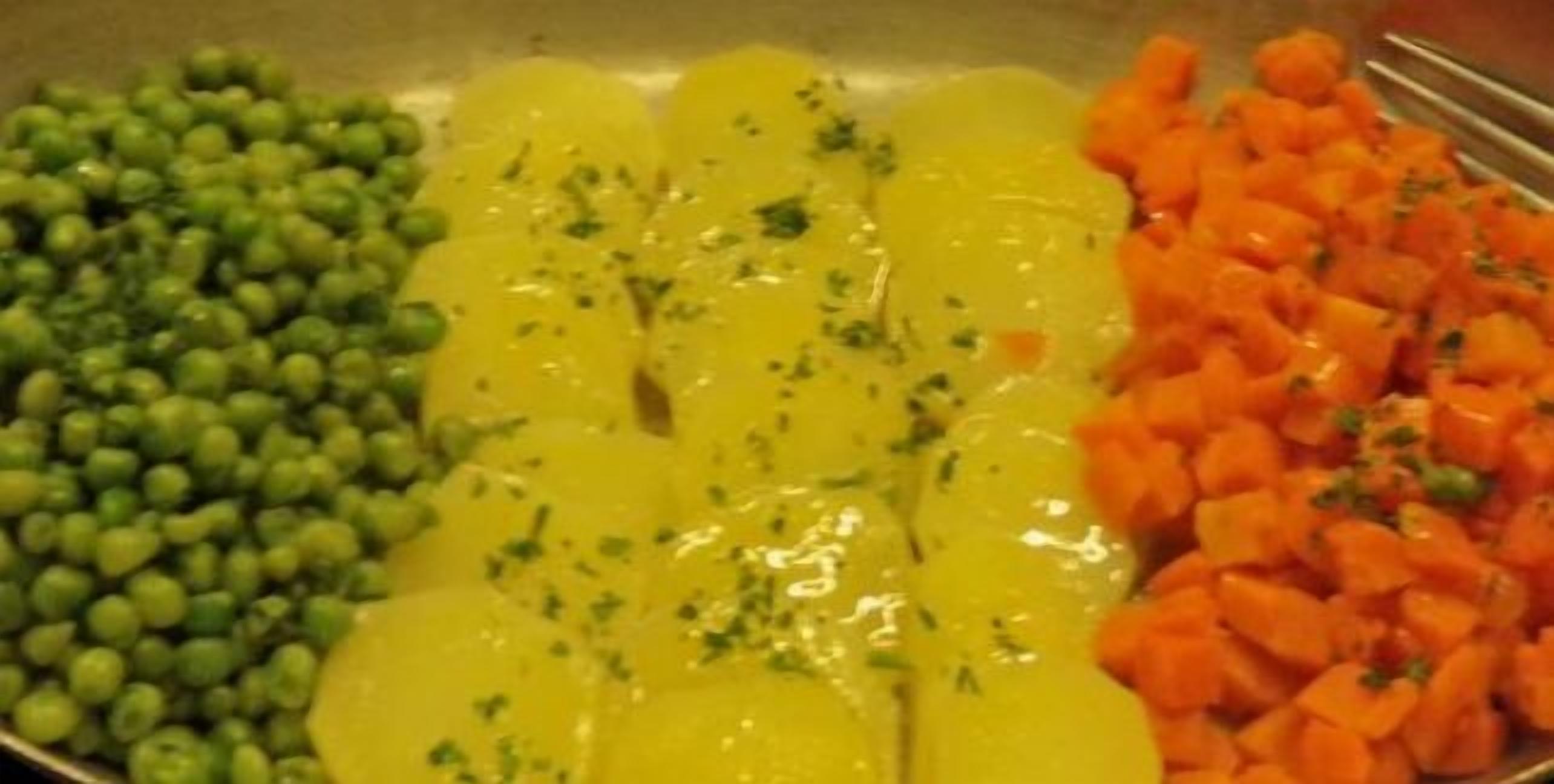 Una sartén con guisantes verdes, salsa amarilla y zanahorias picadas.