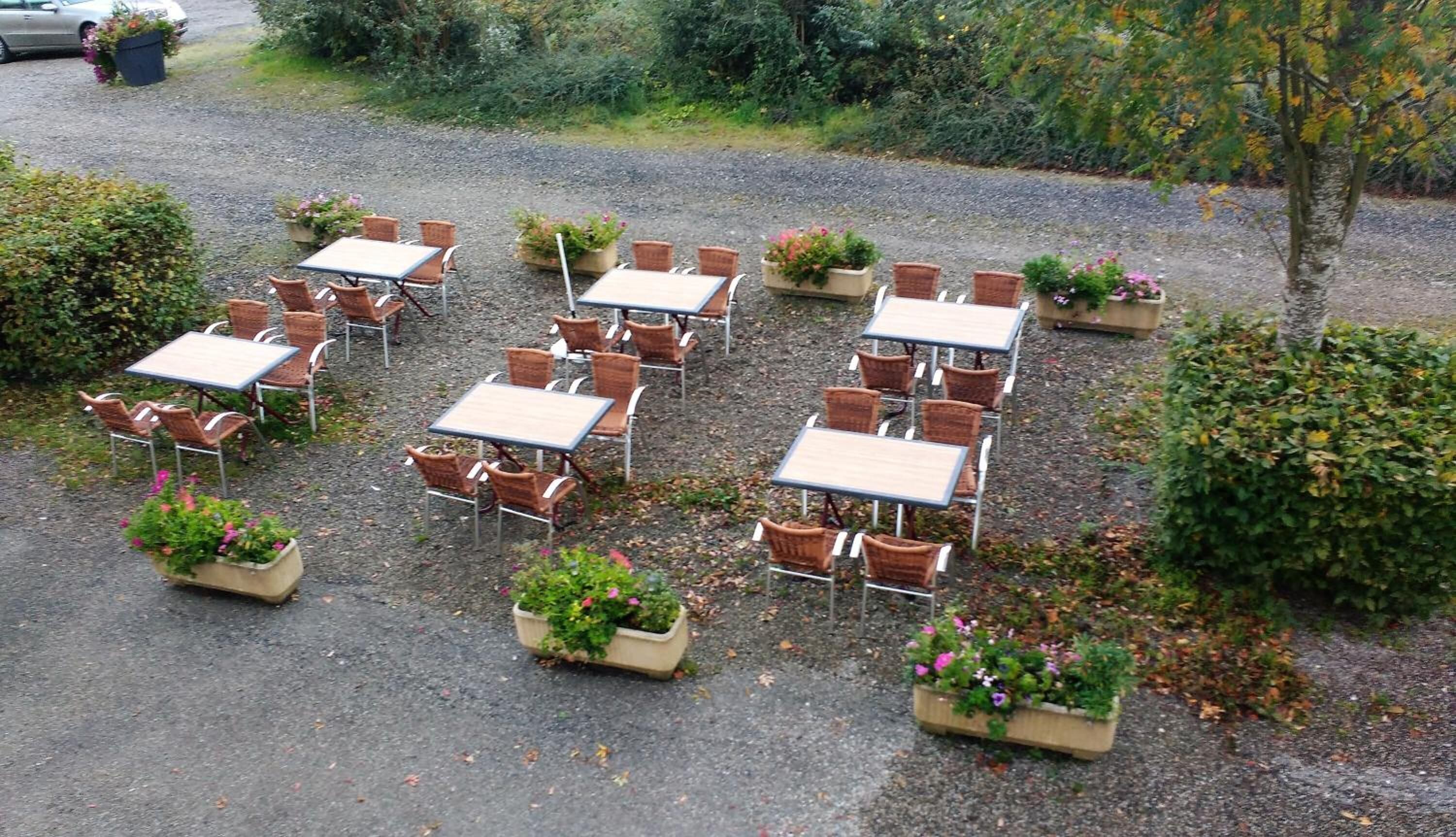 Un espace extérieur aménagé avec des tables et des chaises en osier, entouré de jardinières fleuries.