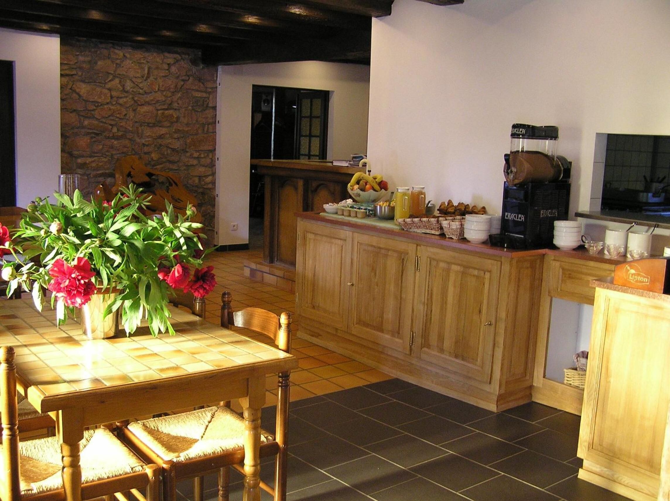 A kitchen with a stone wall, wooden cabinets, a dining table with chairs, and a coffee machine.