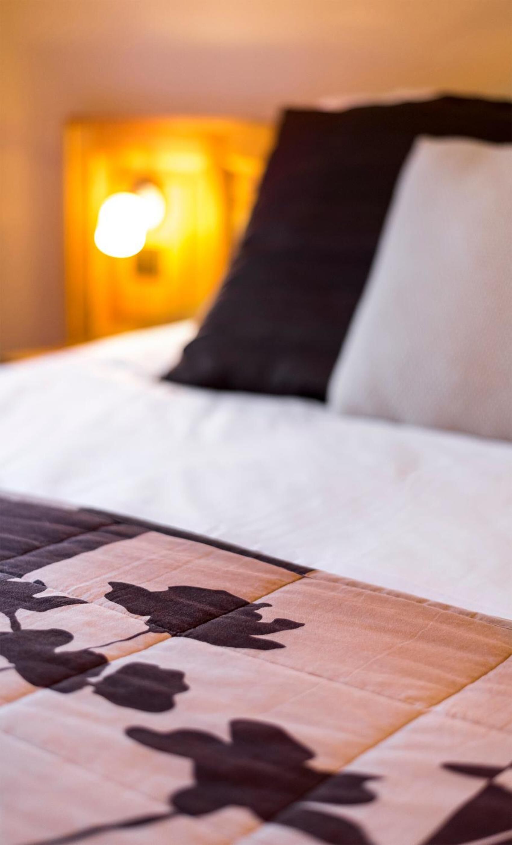 Un lit bien fait, avec une couvre-lit à motifs, un oreiller blanc et un oreiller noir.