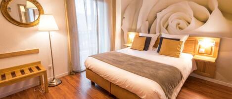 A bedroom with a large bed, wooden floor, a bench, a mirror, and a wall with a floral design.