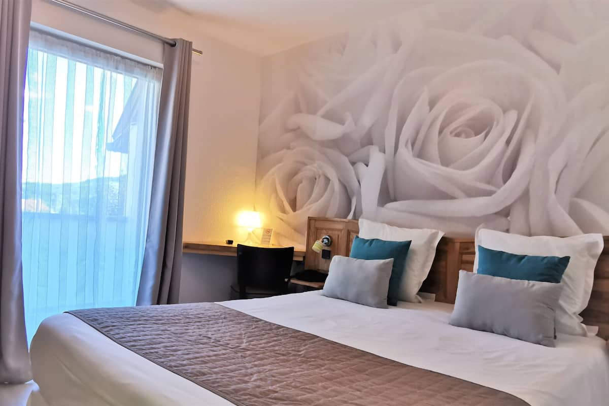 A hotel room with a large bed, a nightstand with a lamp, and a wall mural of roses.