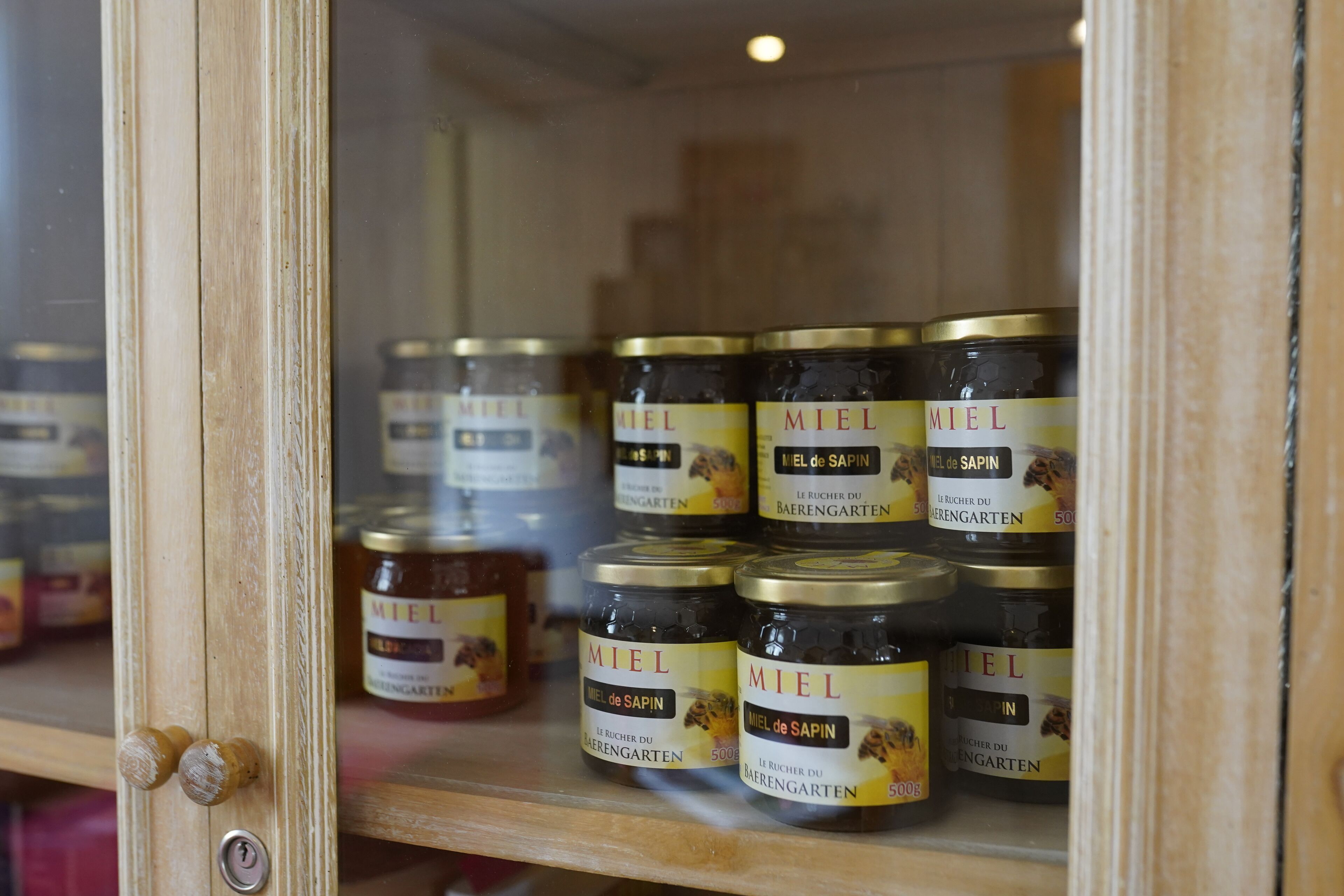 Un armario de madera con puertas de cristal que contiene botes de miel de Sapin.