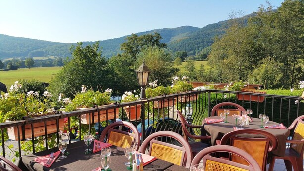 Un espace de restauration en plein air avec des tables et des chaises, une lanterne et une vue sur une vallée verdoyante et des collines.