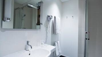 Une salle de bain moderne avec un lavabo blanc, un miroir, une cabine de douche en verre et un porte-serviettes.