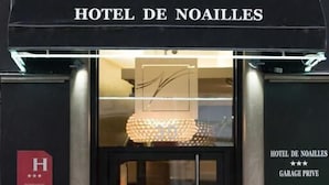 De ingang van Hotel De Noailles met een glazen deur, een bord dat een privégarage aangeeft, en een logo boven de ingang.
