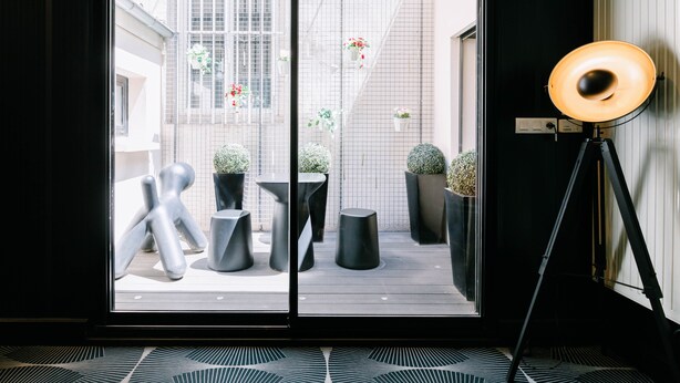 Een modern interieur met een glazen deur die leidt naar een buitenruimte met potplanten en een metalen sculptuur.