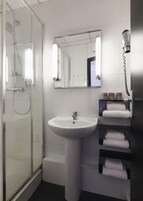 Un bagno con box doccia in vetro, lavabo su piedistallo, uno specchio e un portaserviti con asciugamani piegati.