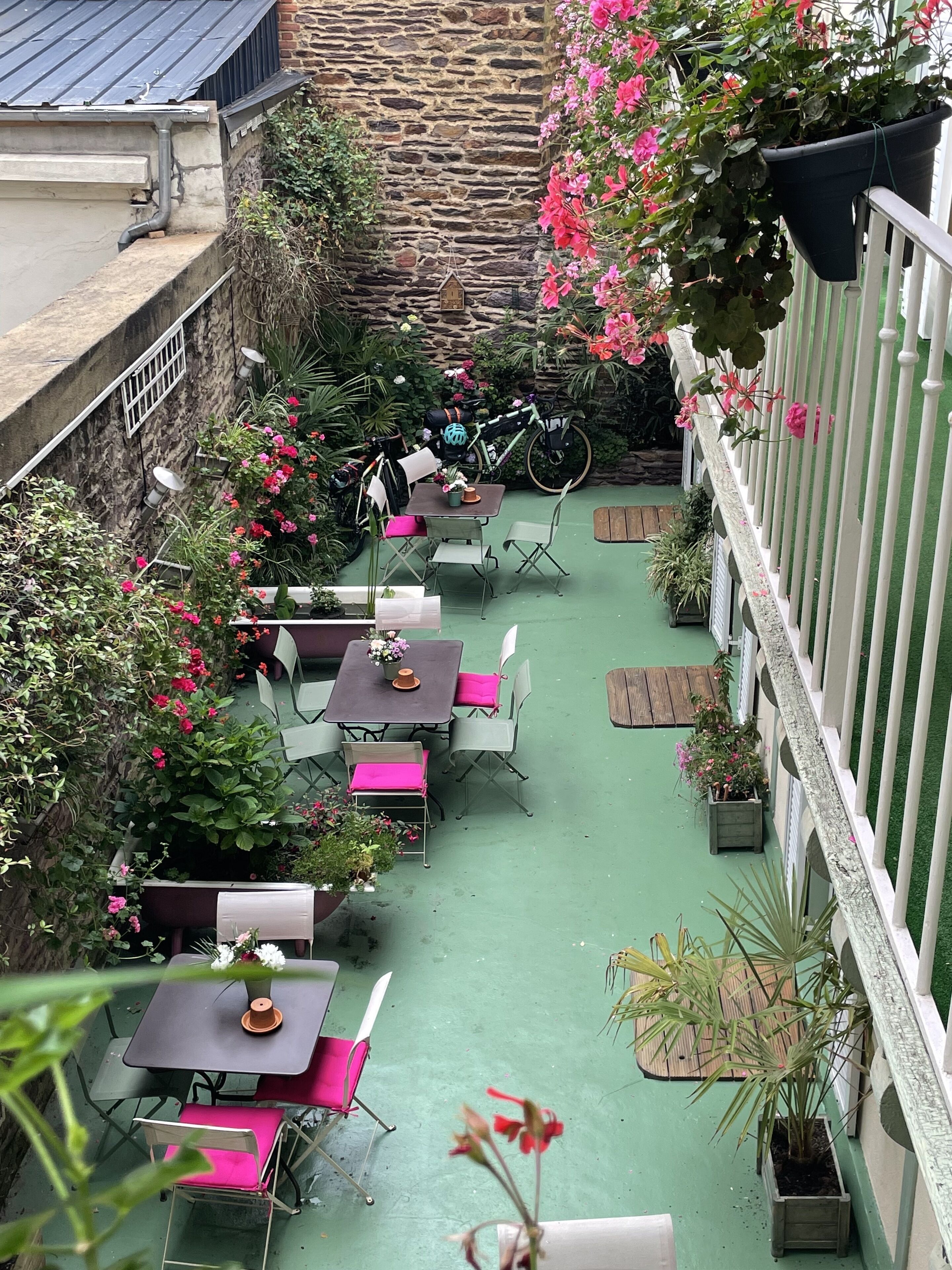 A rooftop patio with tables and chairs, surrounded by potted plants and flowers.