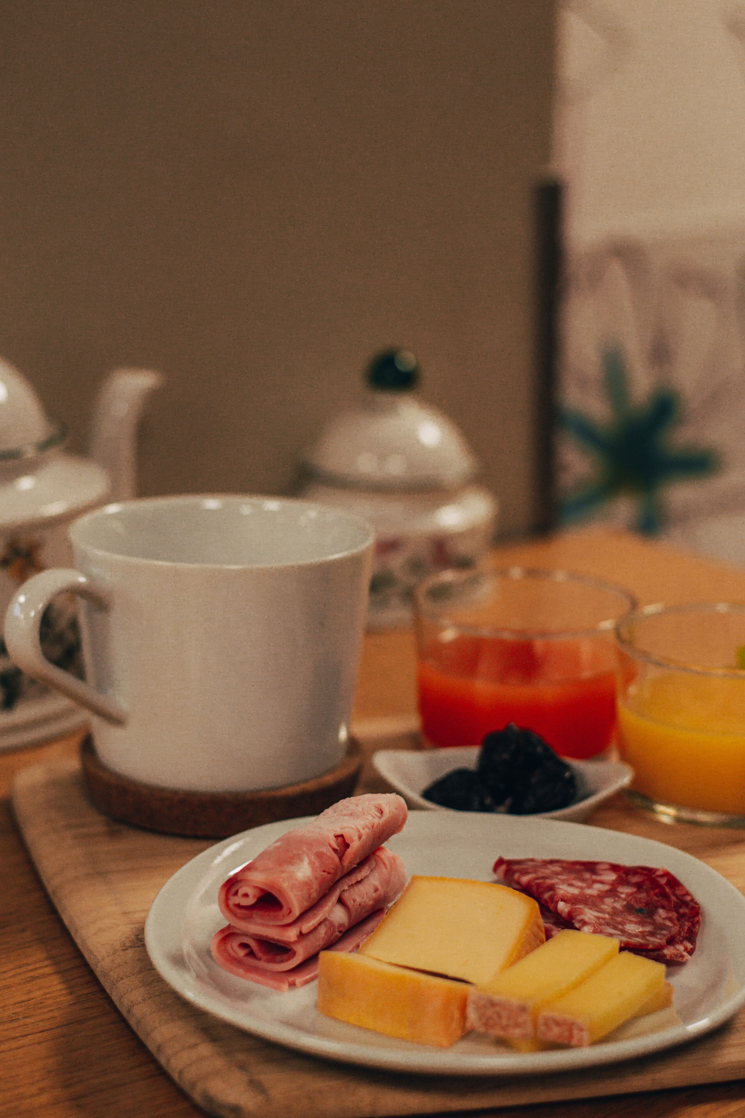 A breakfast setting with a plate of ham, cheese, and salami, a mug, and glasses of orange juice and tomato juice.