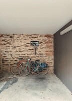 Un área de estacionamiento con dos bicicletas aparcadas junto a un muro de ladrillo. Un cartel encima indica 'RESERVE M2 Garden'.