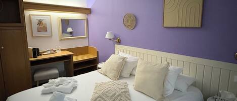 A hotel room with a large bed, a wooden wardrobe, a desk with a lamp, and a small table with a phone.