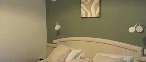 A neatly made bed with towels, a wall-mounted lamp, and a framed abstract painting.