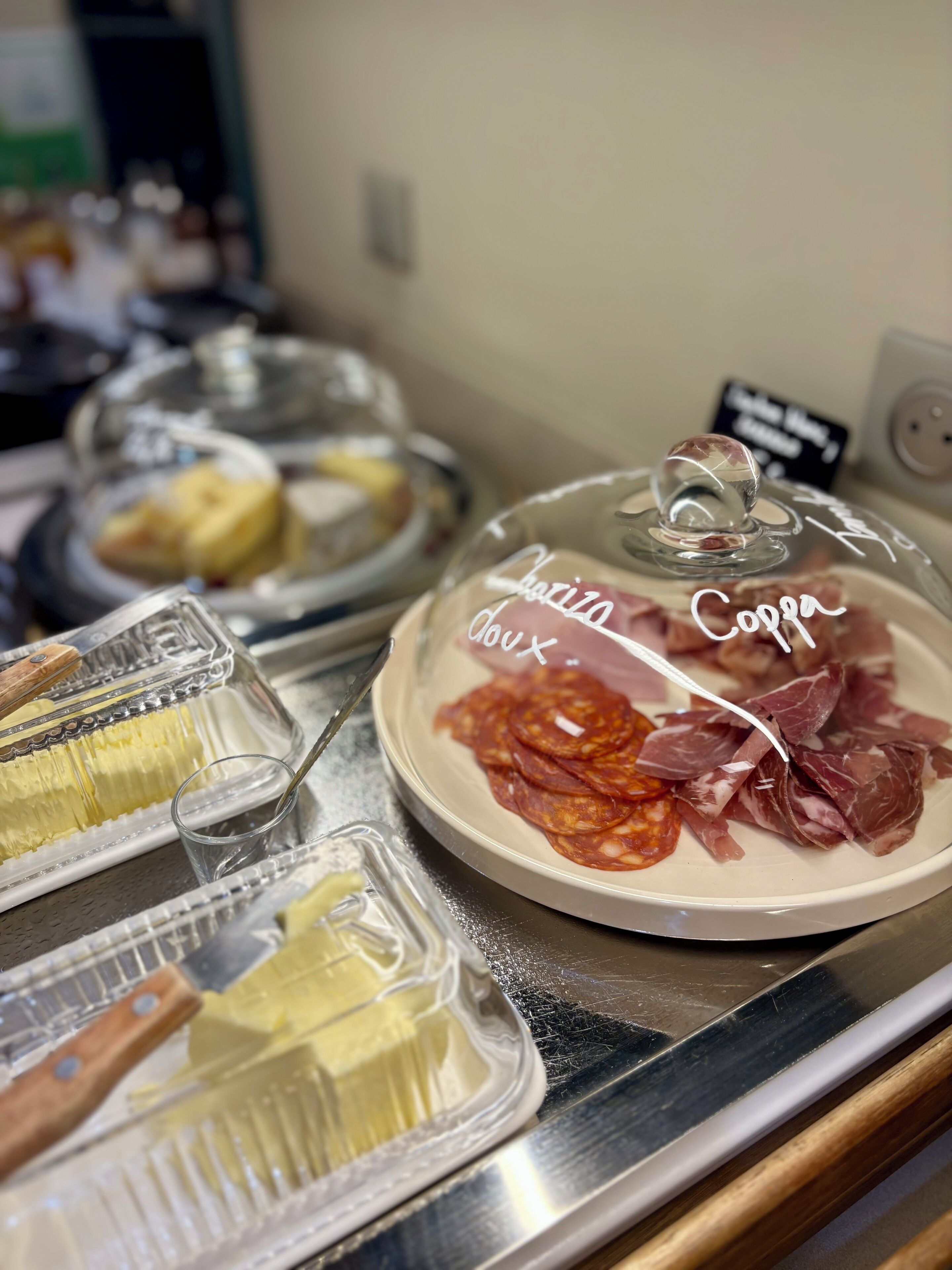 En madpræsentation med forskellige varer, heriblandt en tallerken med teksten "Charizo Coppa" og en glasbeholder med etiket.