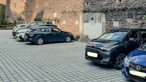 Uma área de estacionamento com carros, um edifício de pedra e céu aberto.