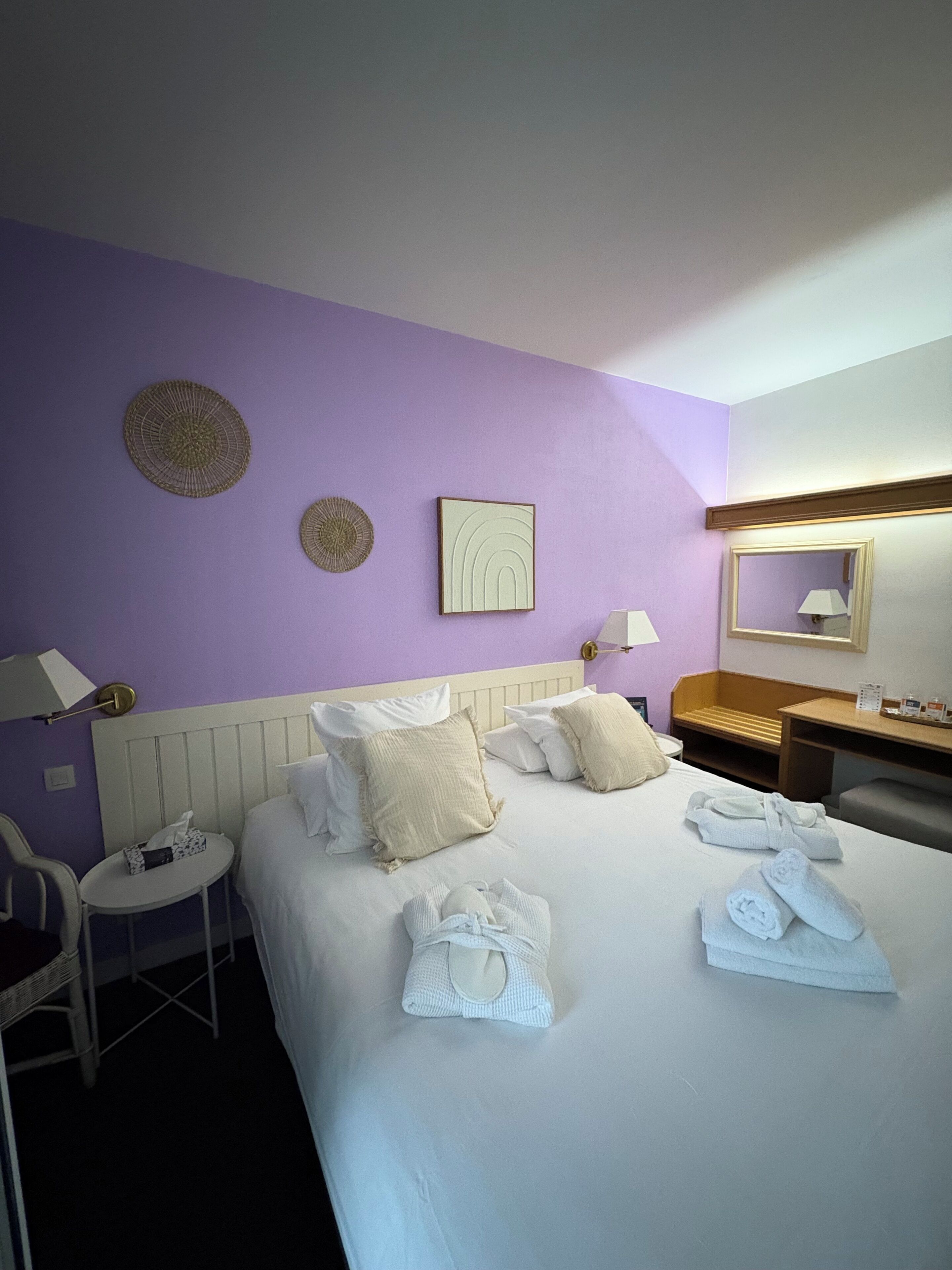 Une chambre d’hôtel comprenant un lit, des oreillers, une table de chevet, une chaise, une lampe et des éléments de décoration murale.