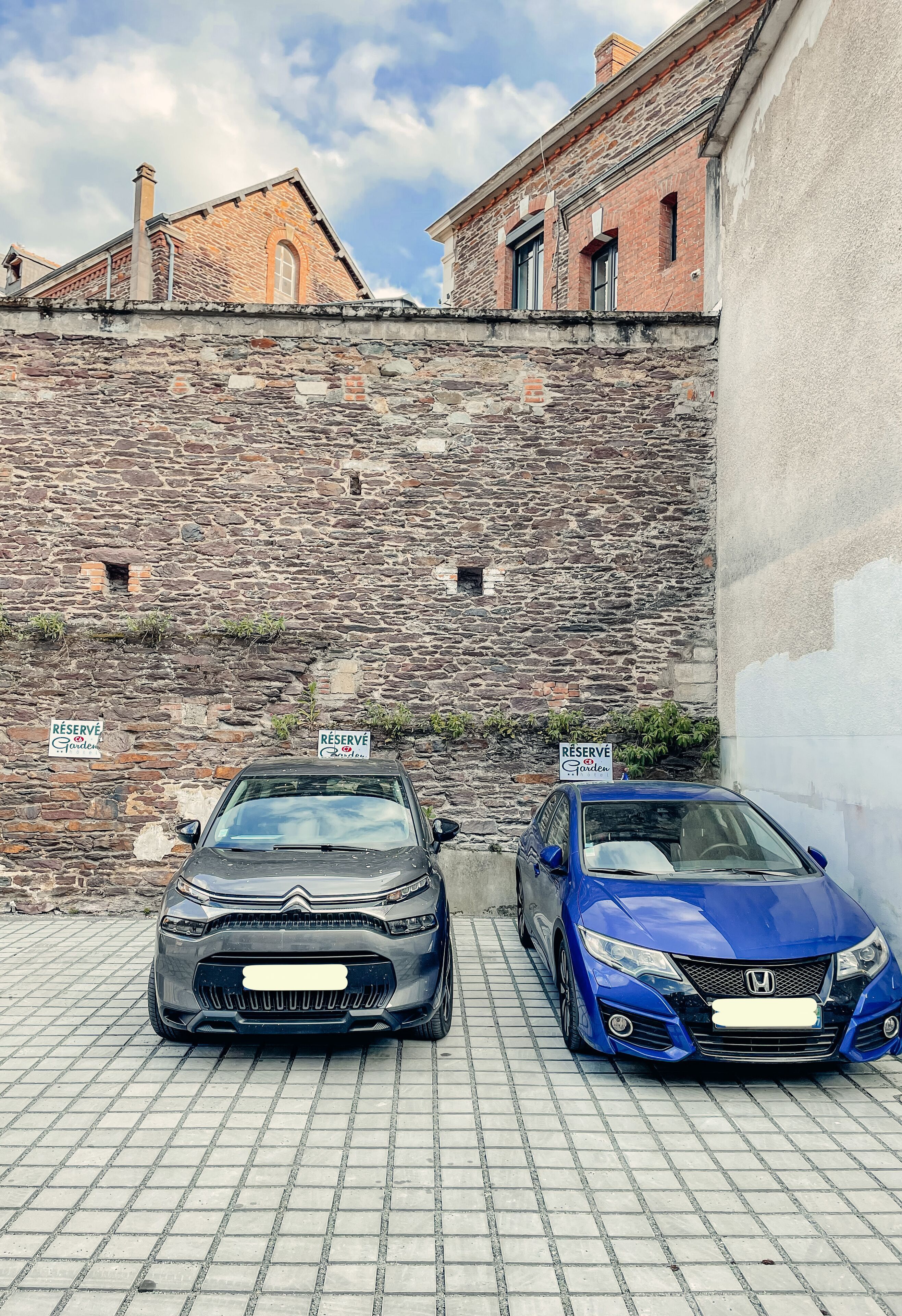 Dos autos estacionados frente a un muro de piedra con letreros que dicen 'RESERVE'.