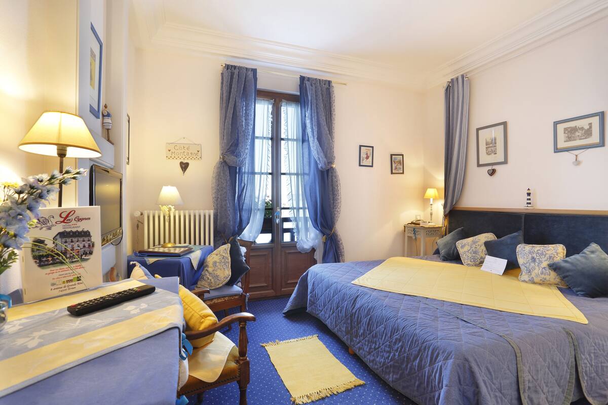 Habitación de hotel con dos camas, un escritorio, una silla, una lámpara y una ventana con cortinas.