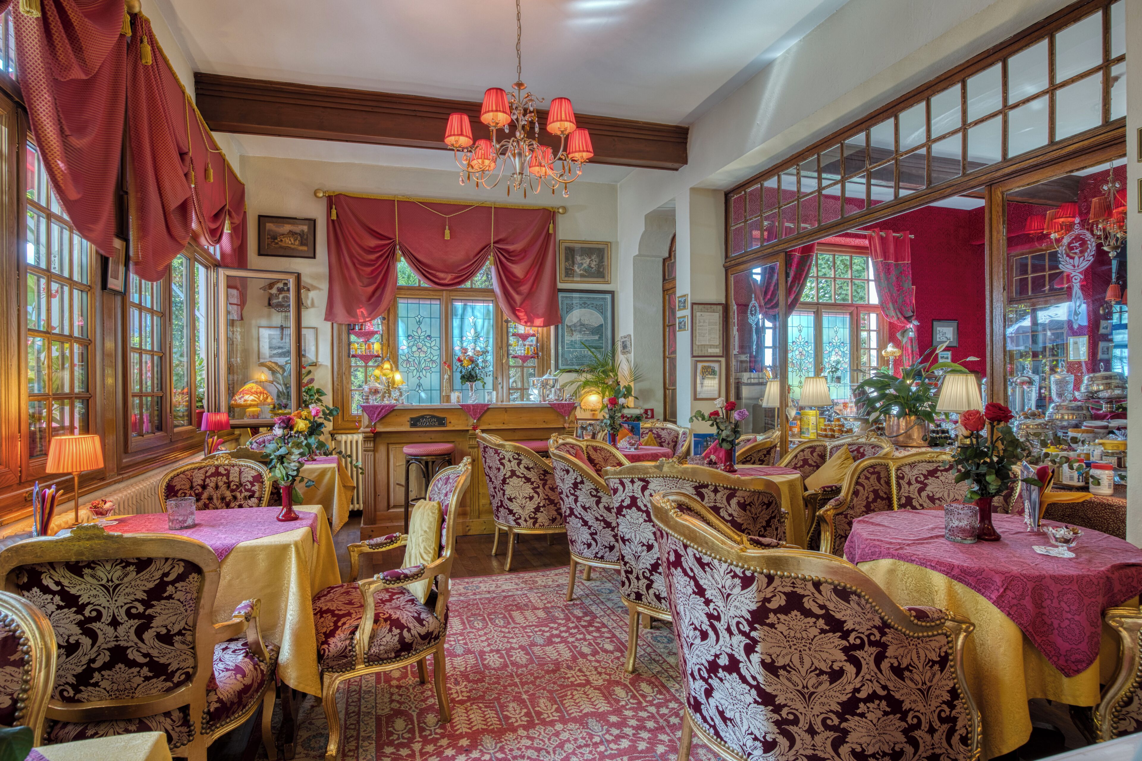 Una habitación con muebles ornamentados, una araña y ventanas amplias con cortinas.