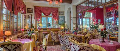 Una habitación con muebles ornamentados, una araña y ventanas amplias con cortinas.