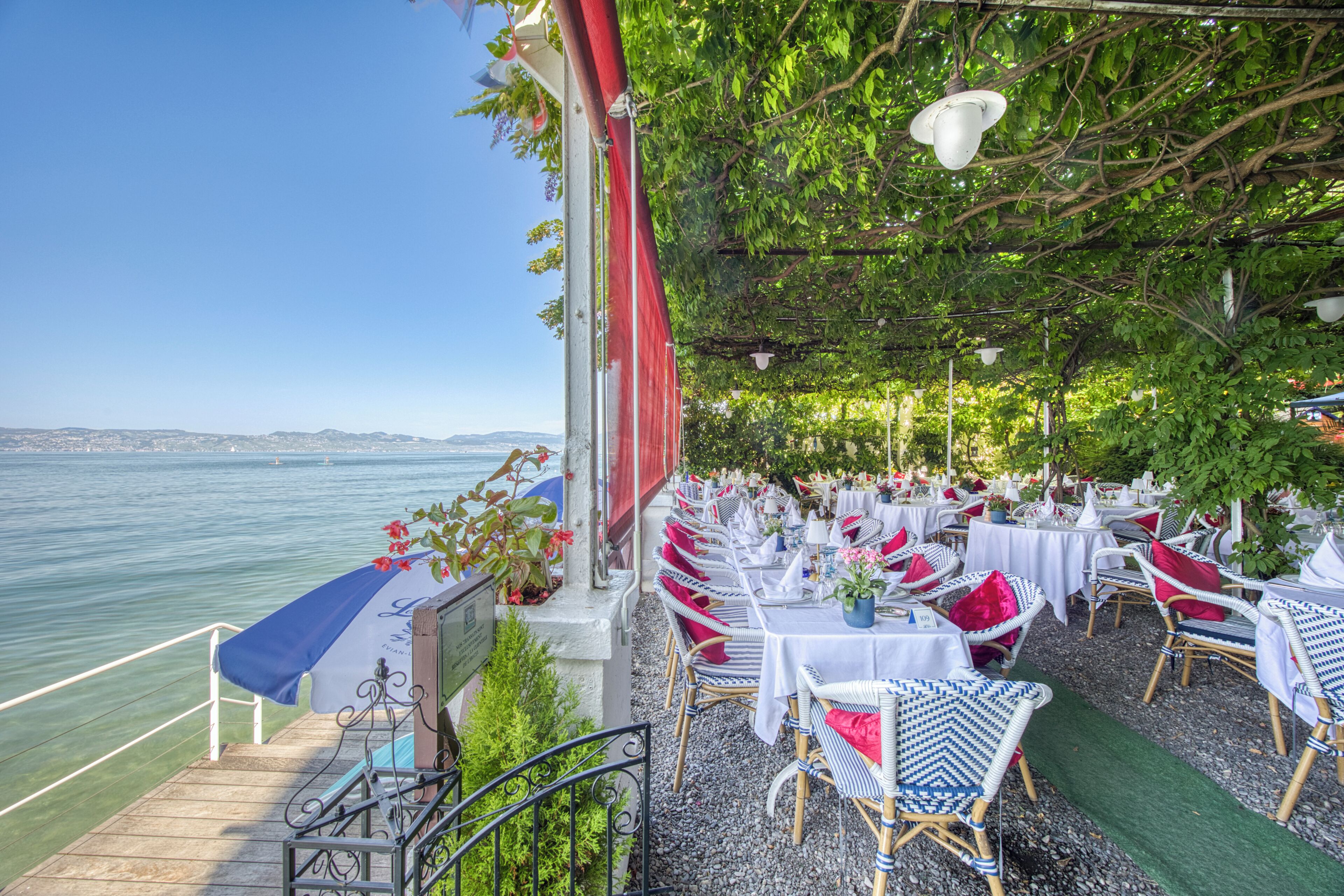 An outdoor dining area with tables and chairs, overlooking a body of water.