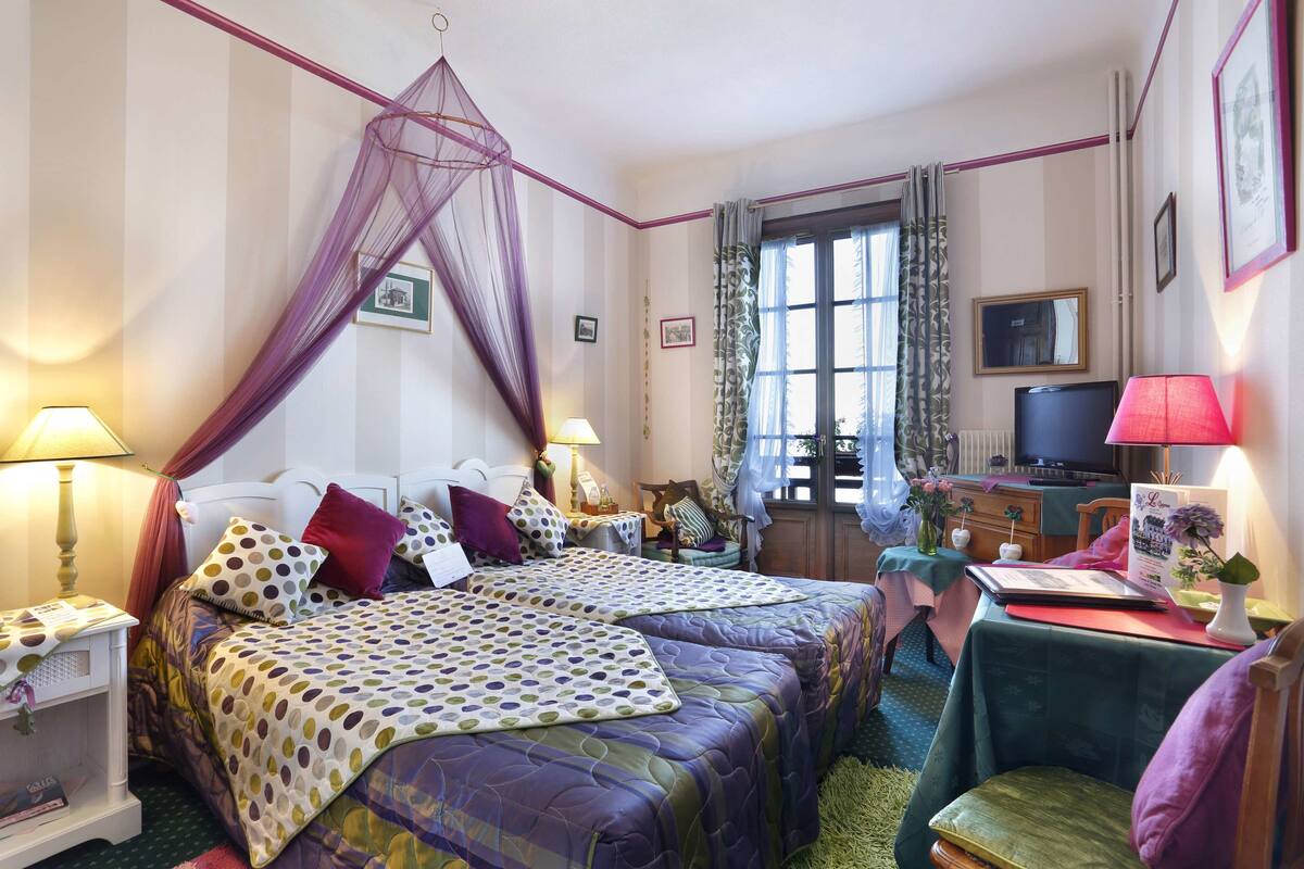 Habitación de hotel con dos camas, televisión, escritorio con lámpara y ventana con cortinas.