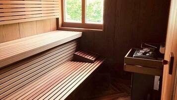 A sauna room with wooden benches, a window, and a small table with items on it.