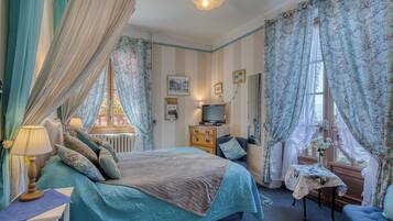 A bedroom with a bed, bedside table, lamp, dresser, TV, and curtains.