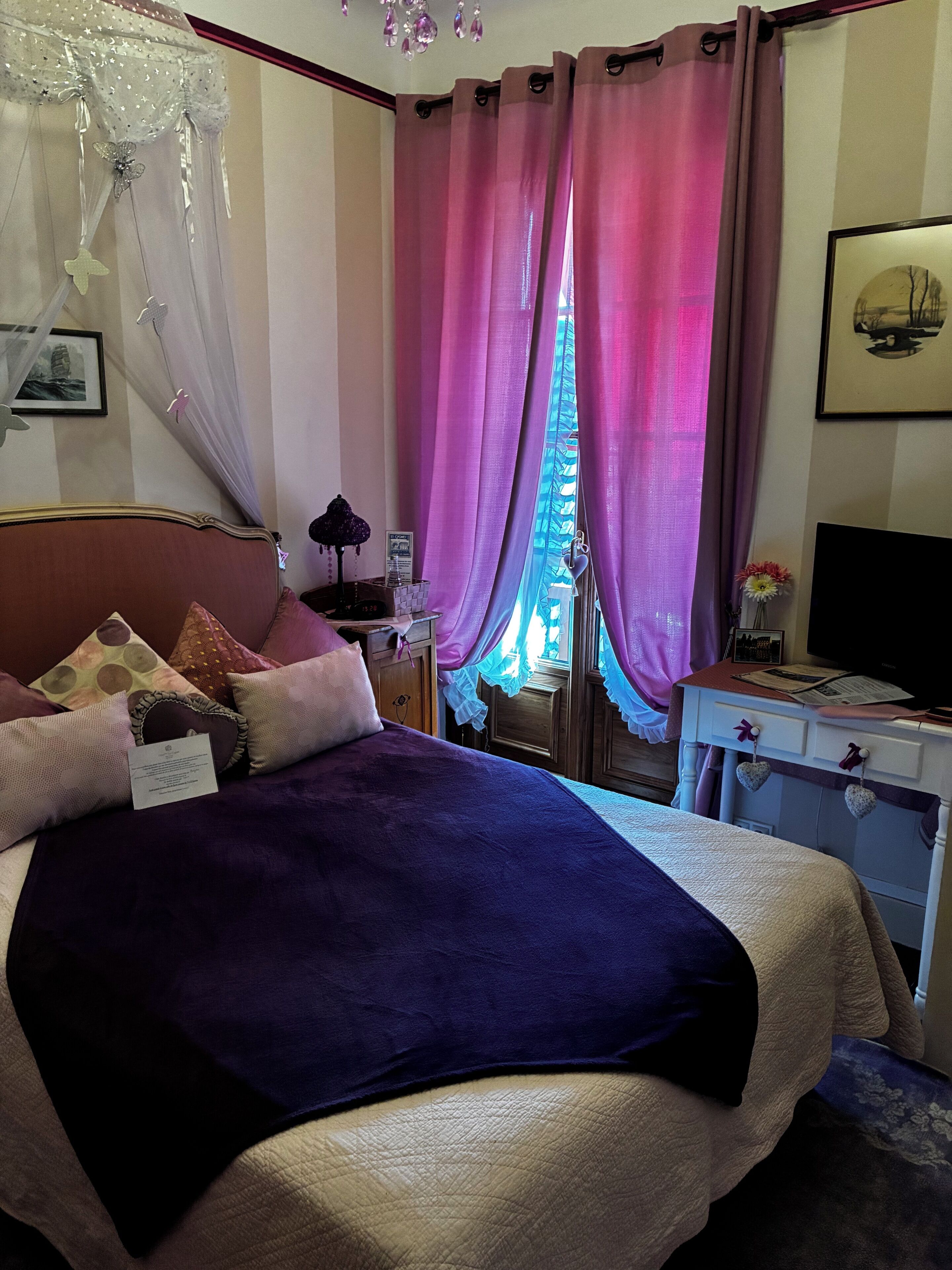 A bedroom with a bed, a nightstand, a television, and a window with curtains.