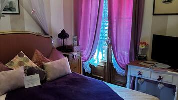 A bedroom with a bed, a nightstand, a television, and a window with curtains.