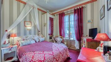 A hotel room with a large bed, a desk with a lamp, a television, and a window with curtains.
