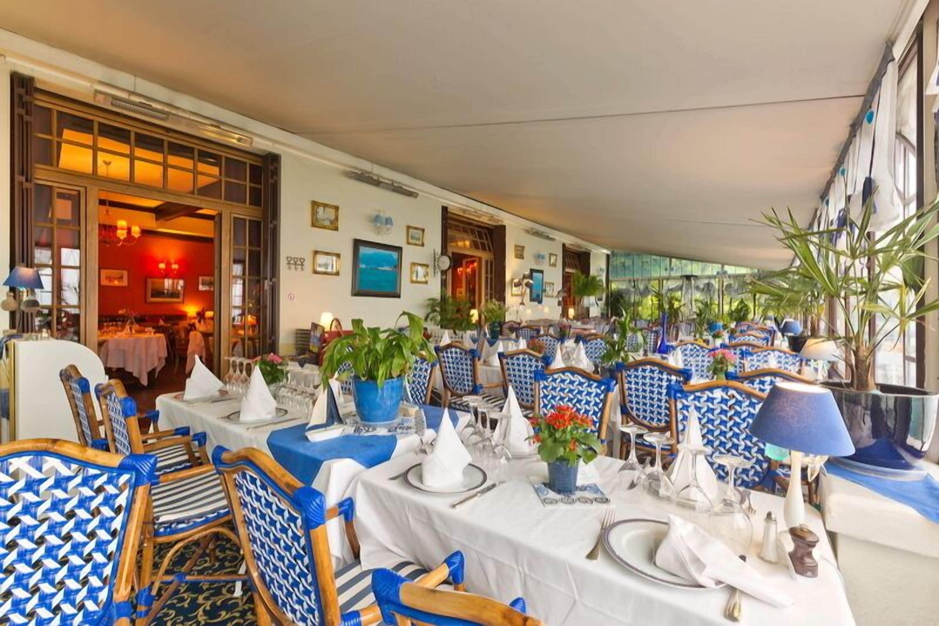 A restaurant with tables set for dining, blue patterned chairs, and potted plants.